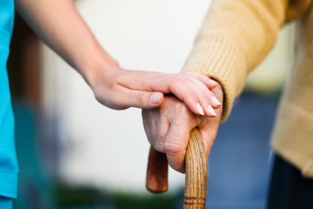younger person's hand on older person's hand with walking cane